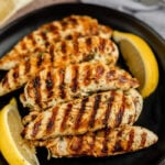Grilled chicken with lemon wedges on black plate, cooked to perfection with grill marks.
