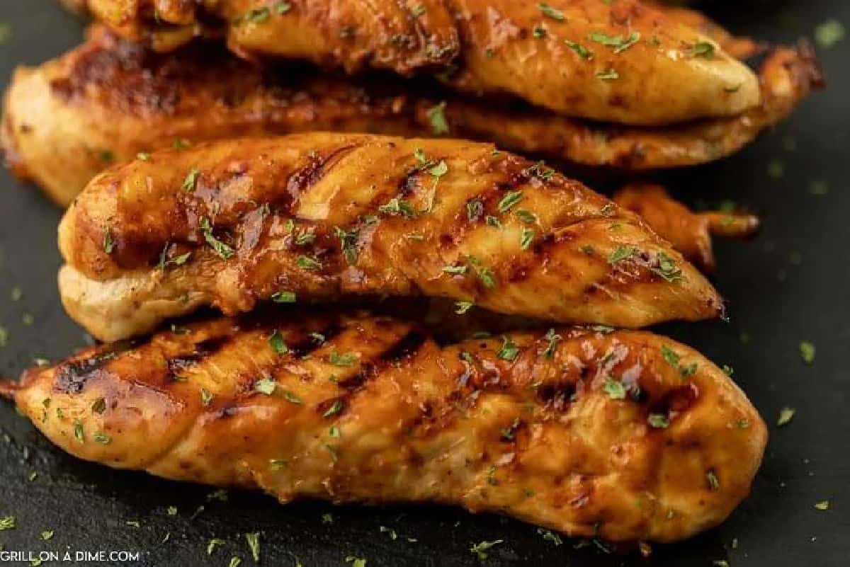 Grilled BBQ Chicken Tenders with visible char marks, garnished with chopped herbs, and arranged on a dark surface.