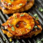 Grilled Pork Chops topped with green onions and pineapple slices on the grill.