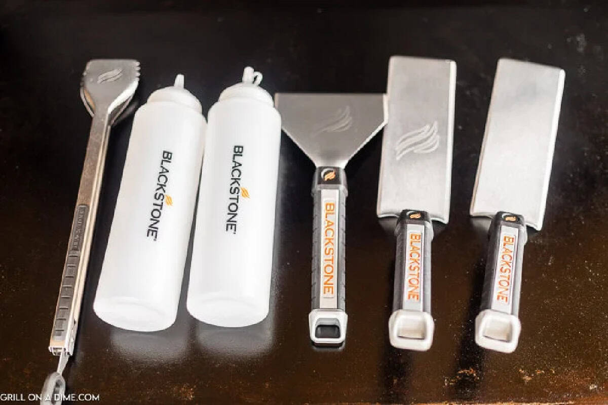 Two white Blackstone-branded squeeze bottles, a spatula, a scraper, a chopper, and a serrated-edge spatula.
