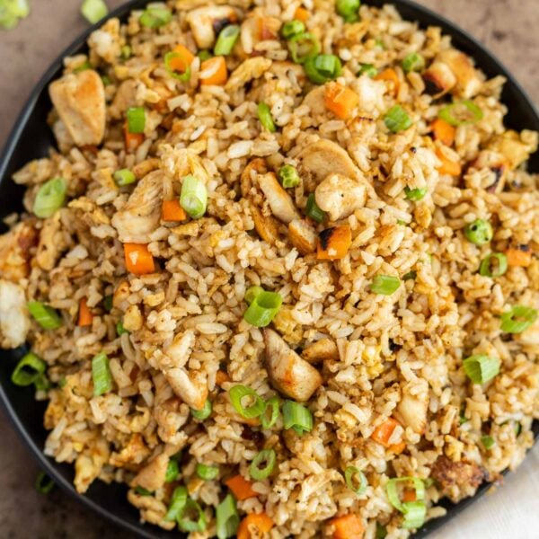 Flavorful chicken fried rice with vegetables in a black serving dish.