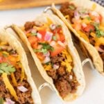 Ground Beef Tacos on a taco stand topped with pico de gallo and fresh cilantro.