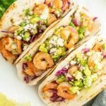 Grilled shrimp tacos with avocado, cabbage, and cheese on flour tortillas.