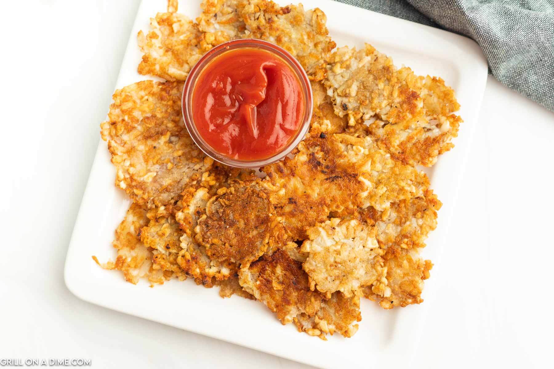 Smashed Tater Tots on a white plate with a small bowl of ketchup