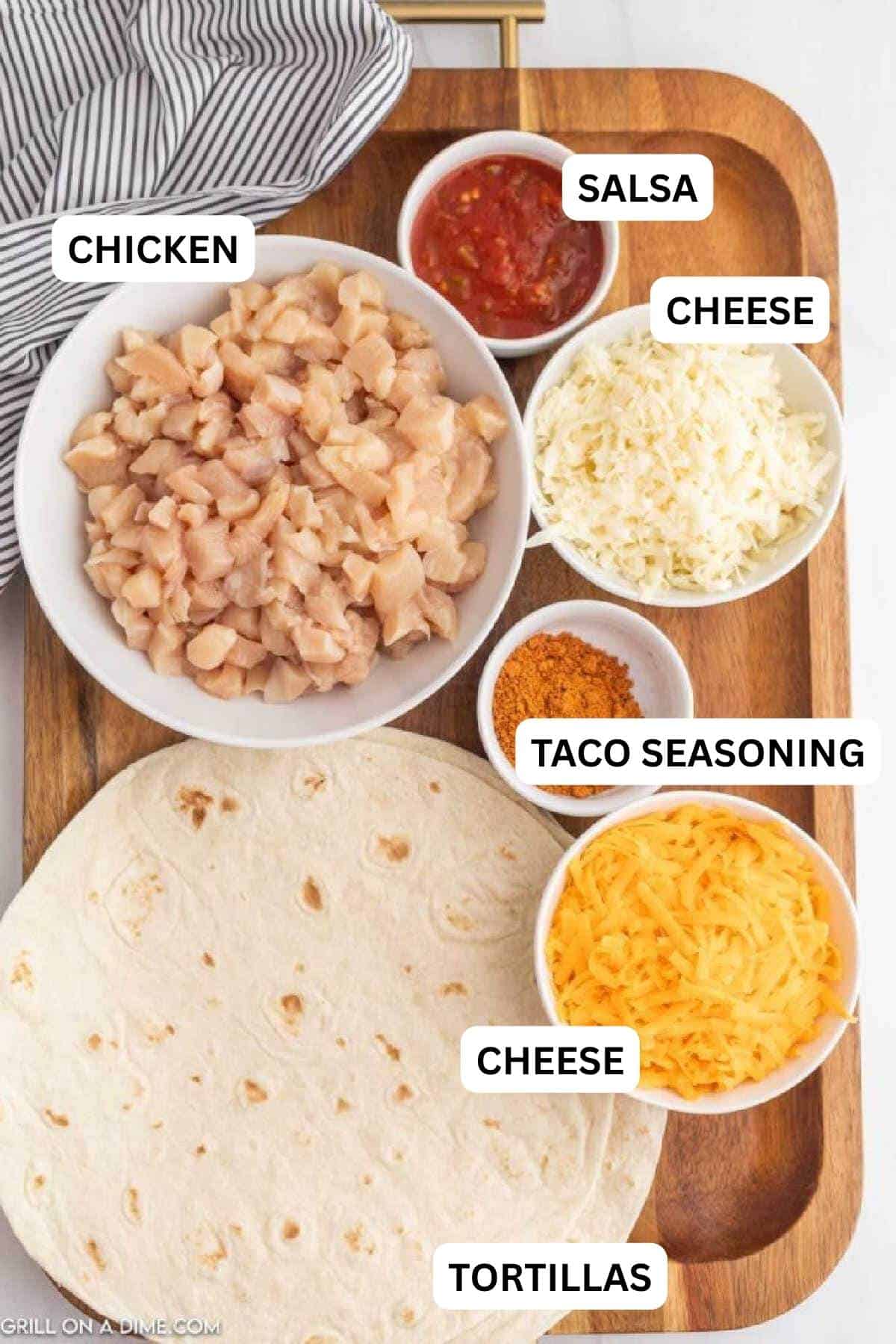 Ingredients needed to make this recipe which includes diced chicken in a bowl with small bowls of salsa, shredded cheese, taco seasoning and flour tortillas.