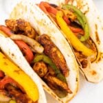 Three flour tortillas filled with seasoned Blackstone Chicken Fajitas—tender chicken strips, sautéed red, yellow, and green bell peppers, plus onions—arranged closely together to showcase vibrant colors and fresh ingredients.