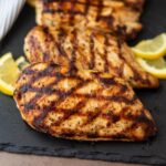 Grilled chicken breasts on a slate board with lemon slices.