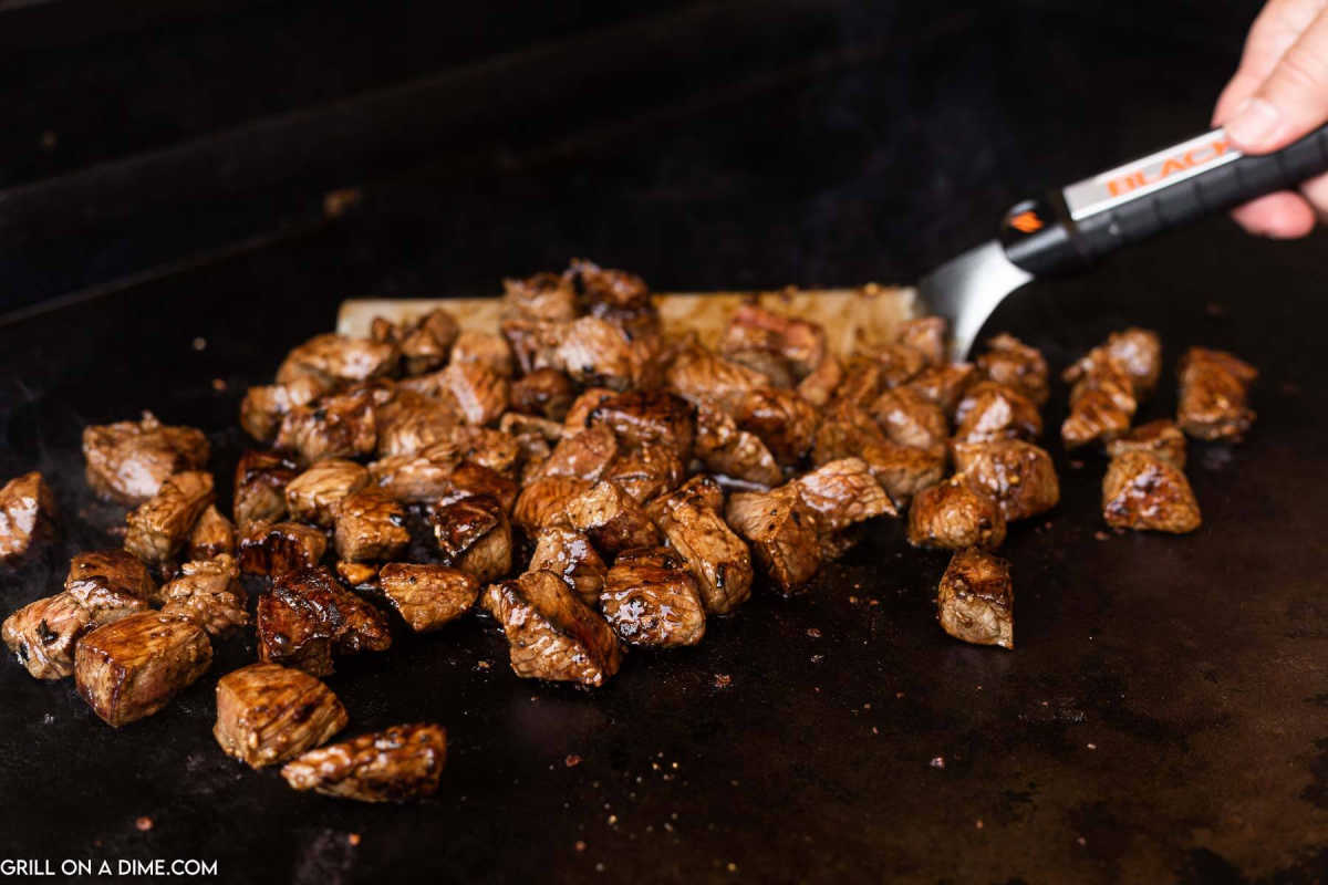 Cooking steak on a Blackstone Griddle with a spatula.