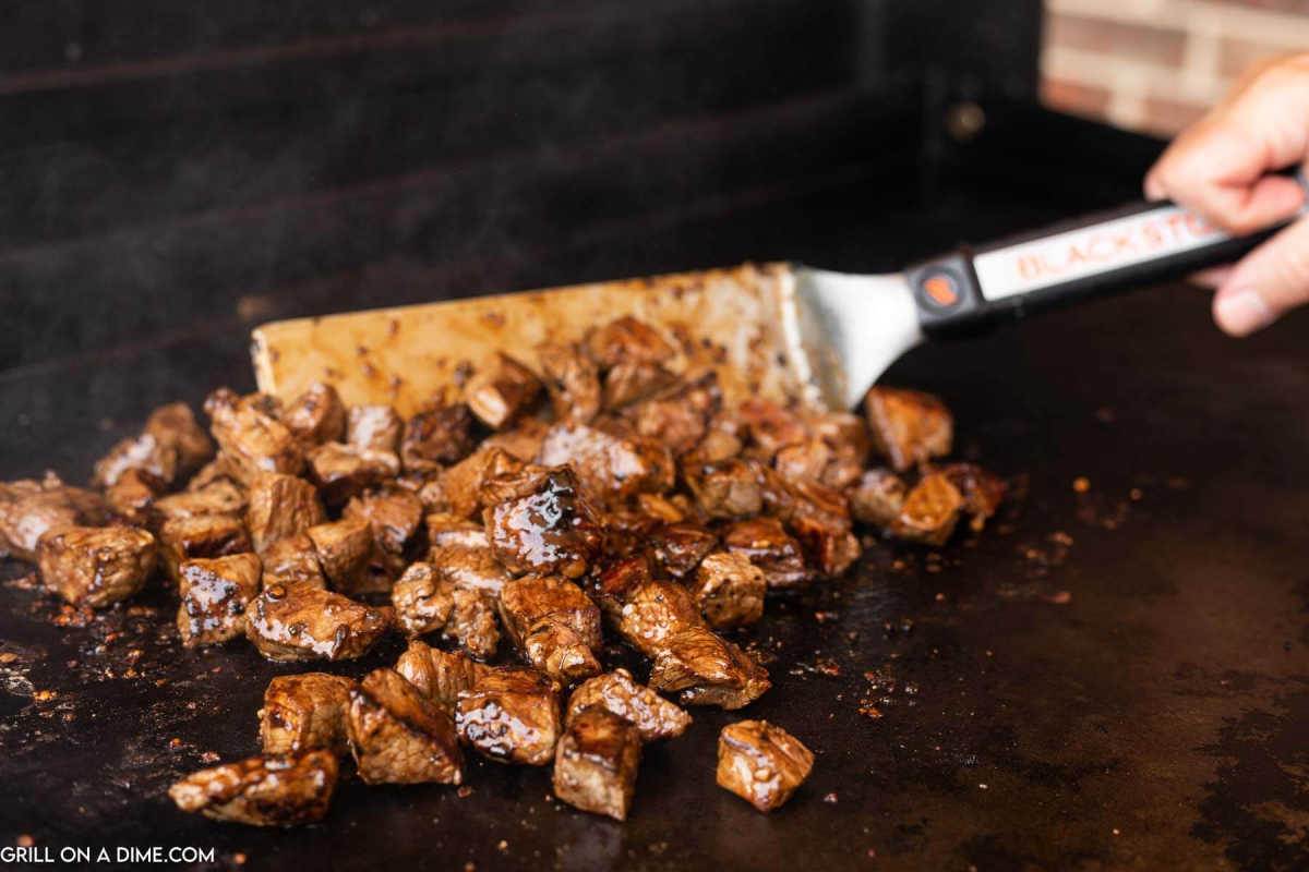 Cooking steak on a Blackstone Griddle with a spatula.