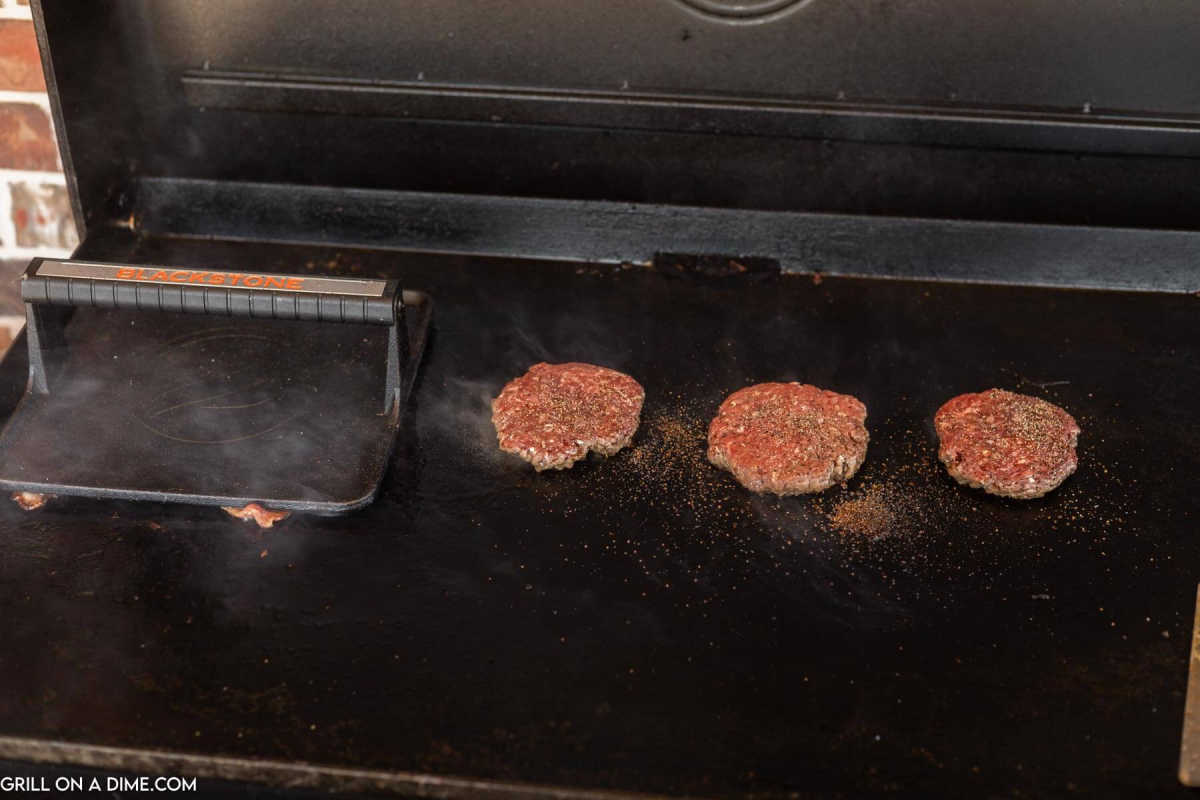 Hamburger patties cooked on the blackstone with a burger press.