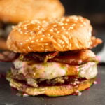 A hamburger with bacon and cheese on a black surface.