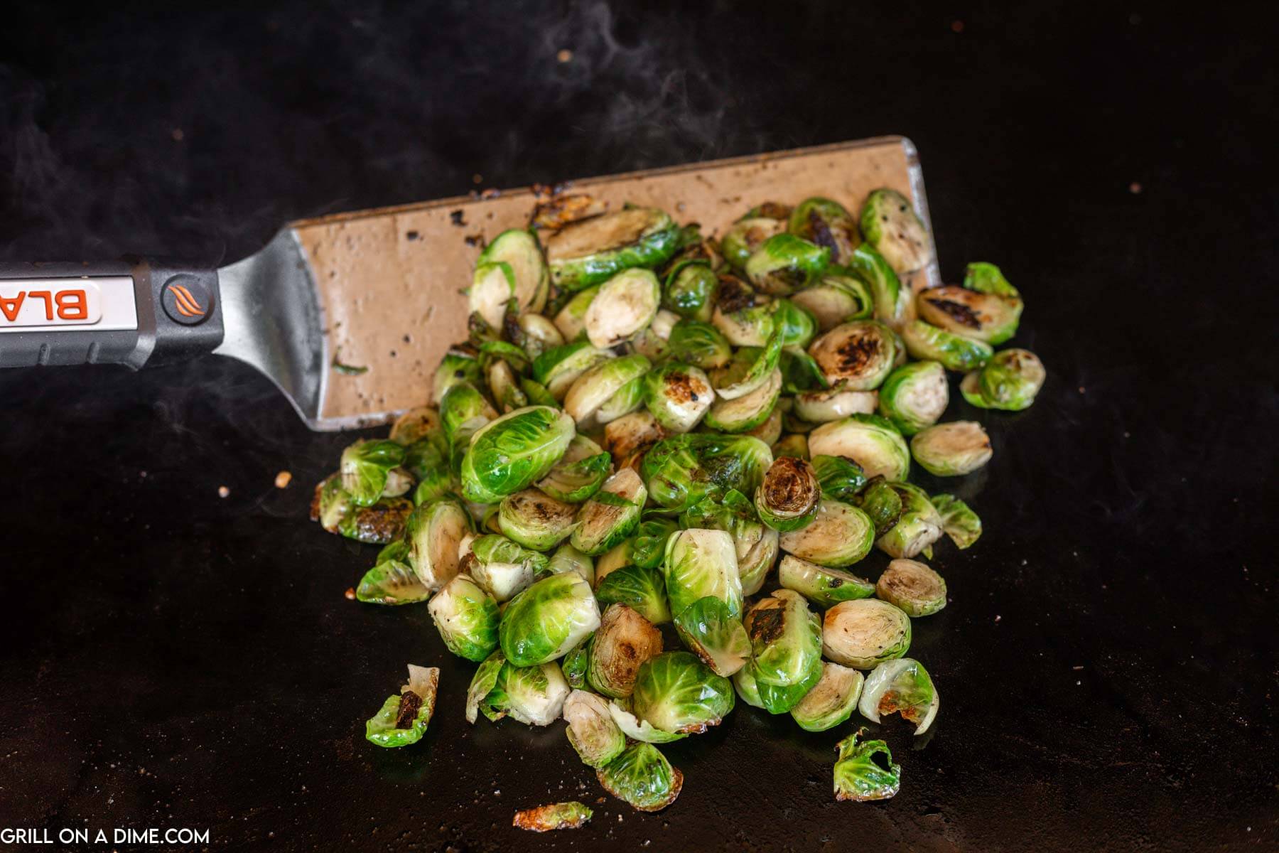 Cooking brussel sprouts on a griddle with a spatula.