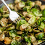 A close-up of Blackstone Brussels sprouts on a plate, with a fork spearing one piece. The Brussels sprouts are browned and crispy, showing a mix of green and golden colors.