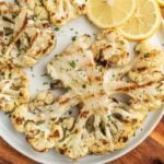 Roasted cauliflower with lemon slices and herbs, healthy vegetable dish for dinner or lunch.