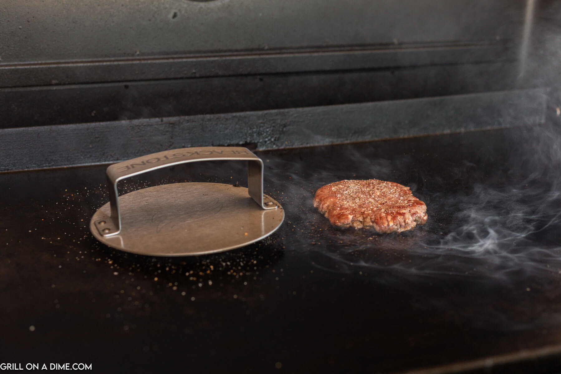 Burger patties being pressed on the griddle with a bacon press.