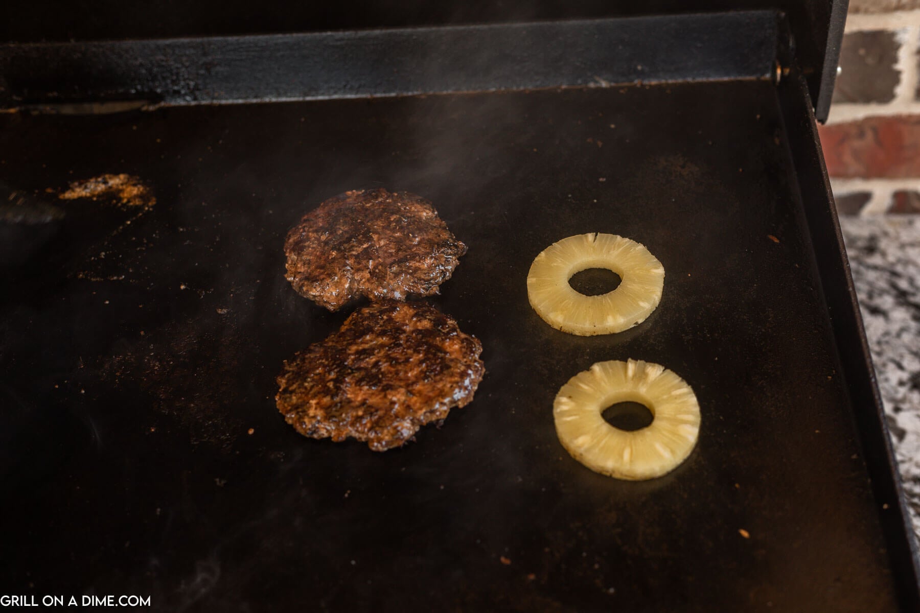 Burger patties and pineapple rings on a blackstone.