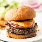 Beef burger with beef patty, cheese, onions, and barbecue sauce on a plate.