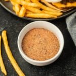 A burger and fries are served with a side of seasoning.