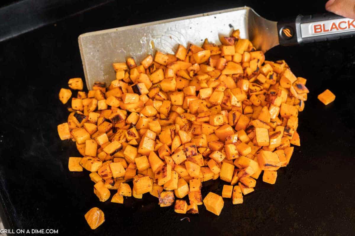 Diced sweet potatoes on a griddle being sauteed with a spatula.