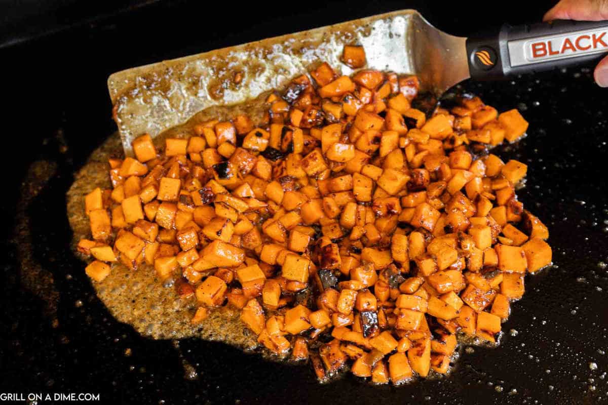 Sautéing the sweet potatoes on the griddle with a spatula.