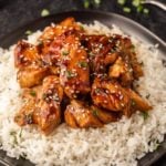 Chicken with sesame seeds and rice on a black plate.