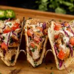 Freshly made grilled fish tacos with vegetables on a wooden serving board.