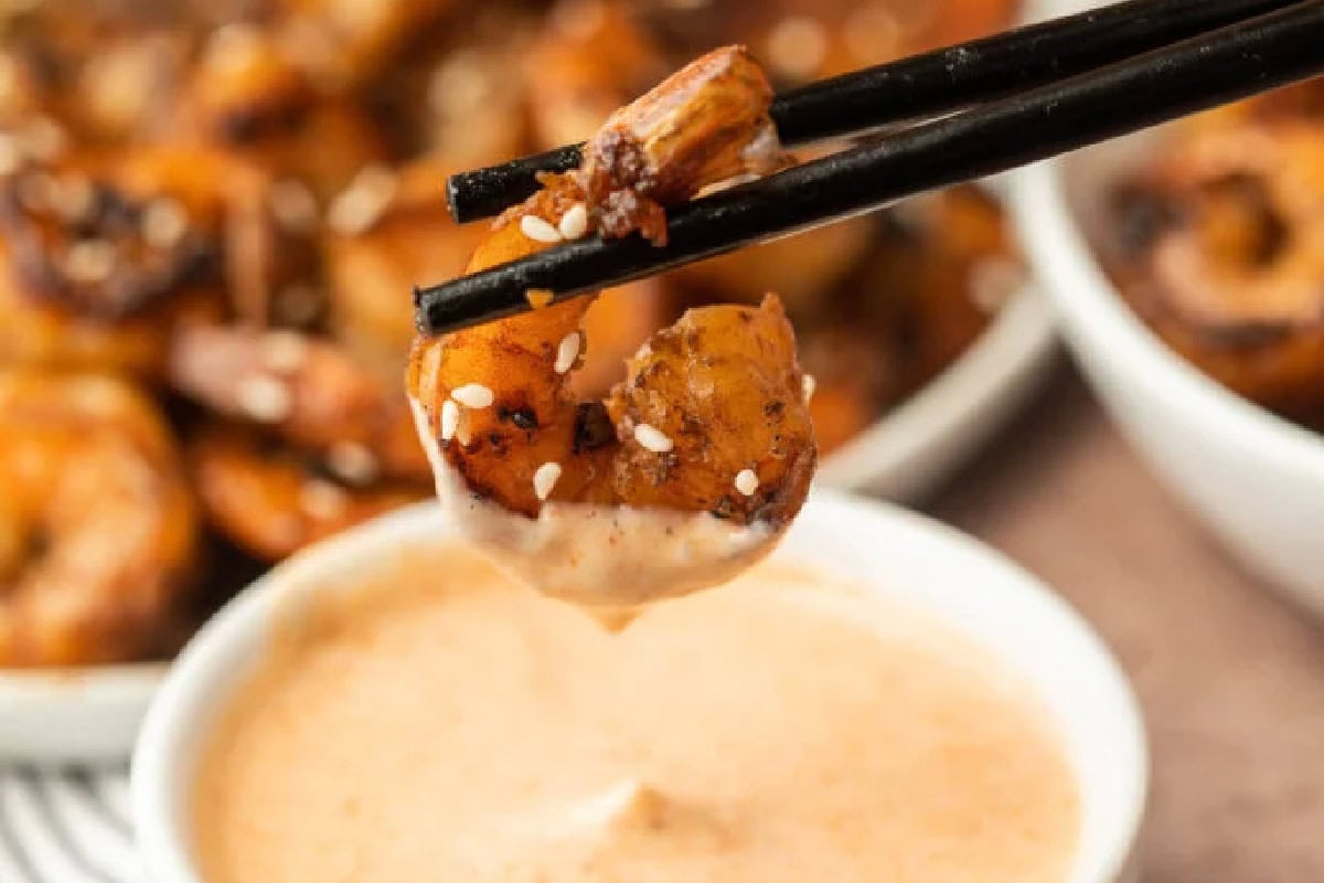 Shrimp being held by chopsticks being dipped into a bowl of yum yum sauce