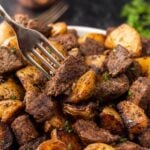 Beef and potatoes in a white bowl with a fork.
