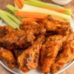 Crispy buffalo chicken wings with fresh celery and carrot sticks on a white plate. Perfect for game day or parties.