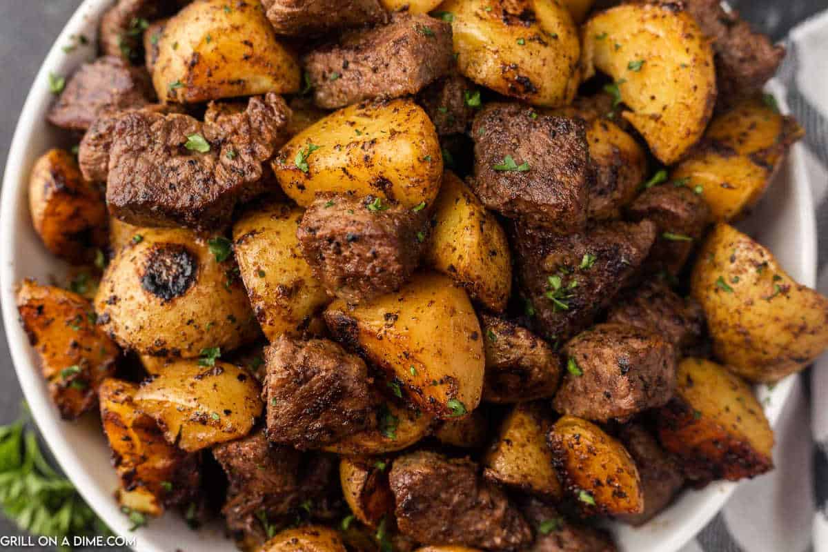 Cooked diced steak and potatoes in a white bowl.