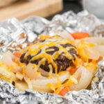 Ground Beef Patties with slice onions and peppers topped with melted cheese in a foil
