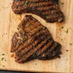 Two steaks on a cutting board with herbs.
