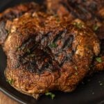 Grilled Portobello Mushrooms on a black platter topped with fresh herbs.