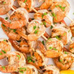 Grilled shrimp skewers on a white plate with lemon wedges.