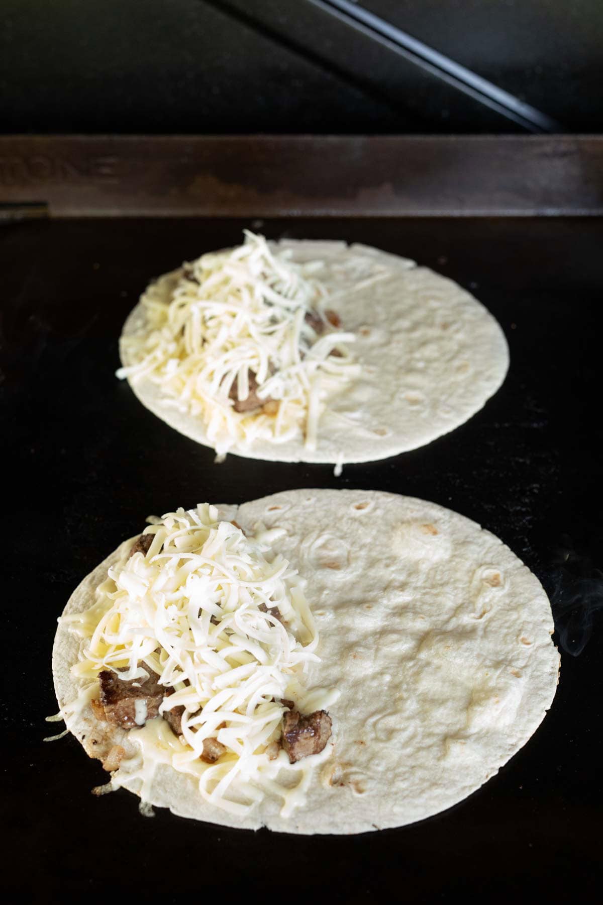 Flour Tortilla on the griddle topped with shredded cheese and steak