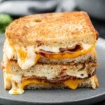 Grilled Cheese with bacon cut in half and stacked on a plate.