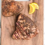 Juicy garlic herb crusted tuna steaks with lemon wedges on wooden cutting board.