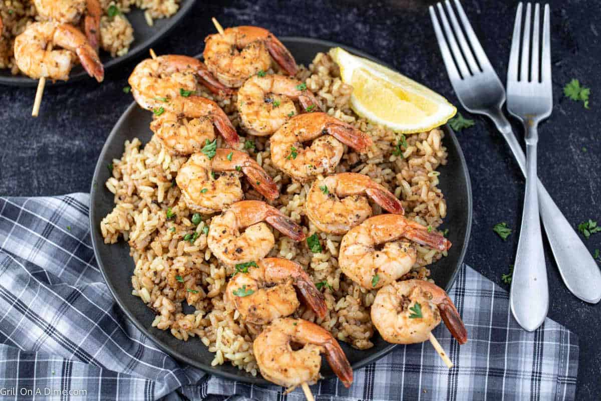 Grilled shrimp skewers on a plate of rice with a fresh lemon on the side.