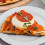 Crispy pepperoni pizza with melted cheese and fresh basil on white plate