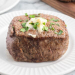 A cooked Blackstone Filet Mignon steak topped with a dollop of melted butter and chopped parsley, served on a white plate.