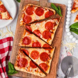 Thin-crust pepperoni pizza on a wooden serving board with fresh basil. Perfect for easy homemade pizza recipes.