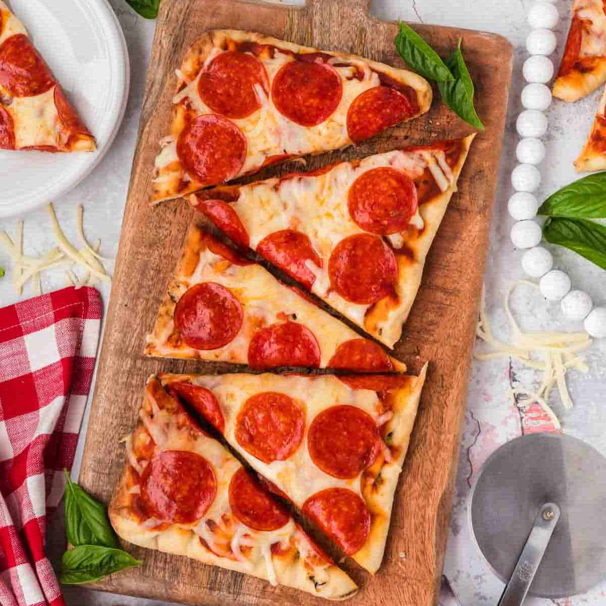 Thin-crust pepperoni pizza on a wooden serving board with fresh basil. Perfect for easy homemade pizza recipes.