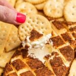 A hand dipping crackers into a cheese and cracker dip.