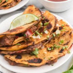 Smash Birria Tacos stacked on a plate and topped with green onions