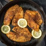 Tilapia in a cast iron skillet with slice lemons on the side