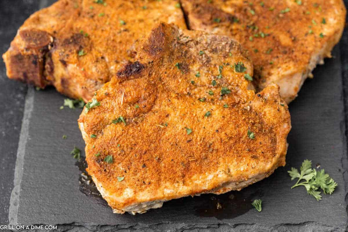 Smoked pork chops stacked on a black platter.