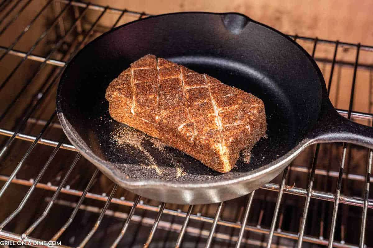 Placing the seasoned cream cheese in a cast iron skillet into the smoker. 
