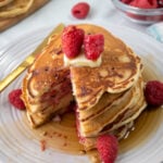 Raspberry Pancakes stacked on a plate topped with syrup and a fresh raspberries