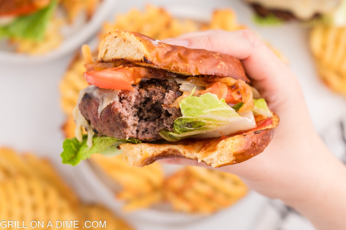 A burger with layers of toppings being held upclose.