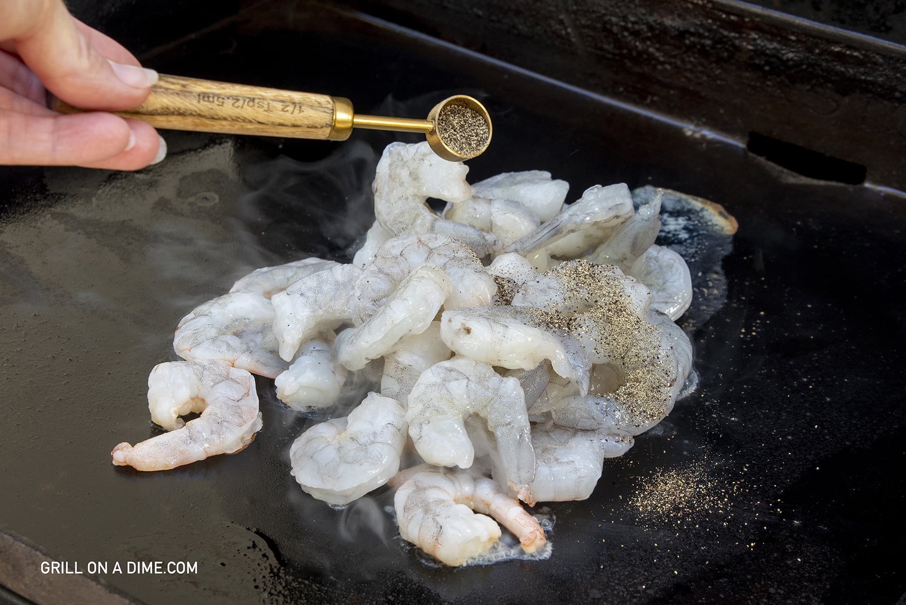 Raw shrimp on the flat top griddle with pepper being sprinkle on top
